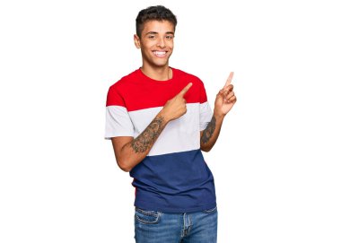 Genç, yakışıklı, Afro-Amerikalı sıradan kıyafetler giyen, gülümseyen ve kameraya bakıp iki elini ve parmağını yana doğru gösteren bir adam.. 