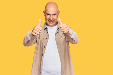 Orta yaşlı kel bir adam, günlük giysiler giyip, olumlu jestler yapıyor, gülümsüyor ve başarı için seviniyor. kazanan jest. 