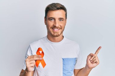 Handsome caucasian man holding awareness orange ribbon smiling happy pointing with hand and finger to the side 