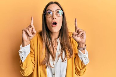 İş stili ve gözlük takan genç ve güzel bir kadın hayret ve şaşkınlık içinde başını kaldırıp parmaklarıyla işaret ediyor ve kollarını kaldırıyordu.. 