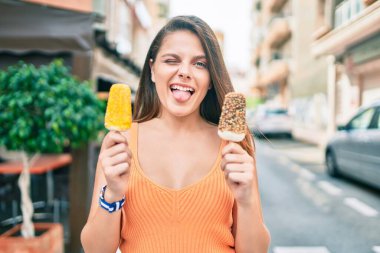 Genç ortadoğulu kız dil ısırıyor ve şehirde dondurma tutuyor..