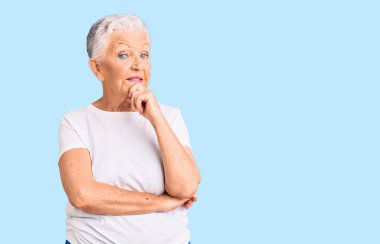 Son sınıf güzeli, mavi gözlü, gri saçlı, sıradan beyaz tişörtlü, kameraya kendinden emin, çapraz kollu ve çeneli bir şekilde gülümseyen bir kadın. Olumlu düşünmek. 