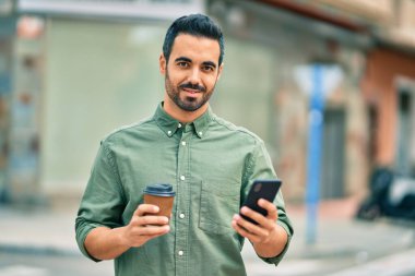 Genç İspanyol adam şehirde akıllı telefon kullanarak mutlu gülümsüyor..