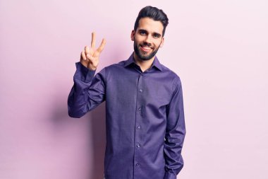 Sakallı, rahat gömlekli, gülümseyen, parmaklarını zafer işareti yaparken gösteren genç ve yakışıklı bir adam. İki numara.. 