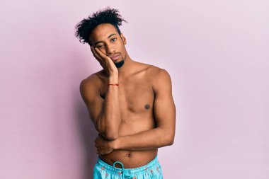 Sakallı, mayo giymiş, depresyondan sıkılmış, yorgun ve kollarını kavuşturmuş genç Afrikalı Amerikalı bir adam.. 