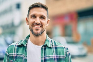 Genç beyaz adam gülümseyerek şehirde mutlu mesut duruyor..