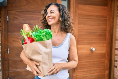 Orta yaşlı İspanyol kadın, elinde alışveriş torbalarıyla şehirde mutlu bir şekilde gülümsüyor..
