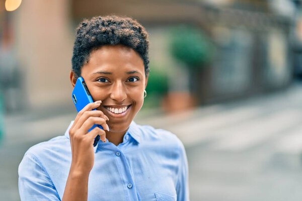 Молодая африканская американка улыбается счастливо разговаривая по смартфону в городе.