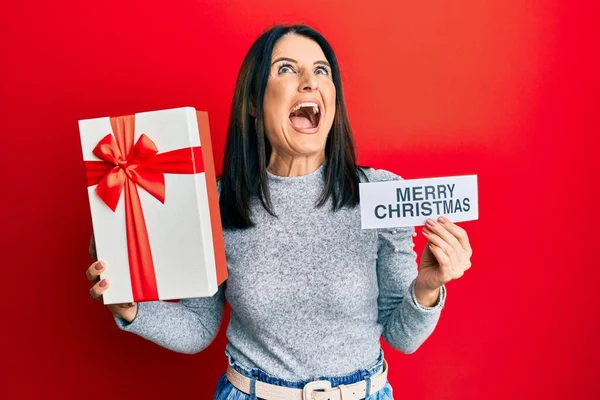 Middle Age Brunette Woman Holding Merry Christmas Message Gift Angry — Stockfoto