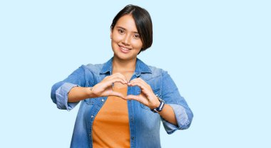 Kısa saçlı, sıradan bir kot ceket giyen, aşık gülümseyen ve elleriyle kalp sembolü yapan genç, güzel bir İspanyol kadın. romantik kavram. 