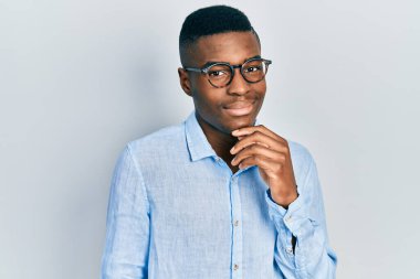 Sıradan kıyafetler ve gözlüklerle gülümseyen genç Afro-Amerikalı adam kameraya kollarını kavuşturup çenesini kapatarak bakıyor. Olumlu düşünmek. 