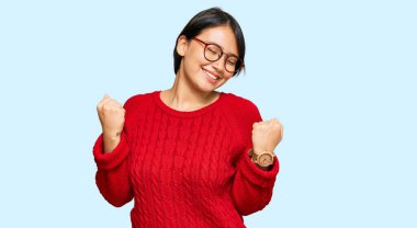 Kısa saçlı, sıradan süveter giyen, gözlüklü, çok mutlu ve heyecanlı genç İspanyol bir kadın kolları havada, gülümseyerek ve başarı için çığlık atarak zafer jesti yapıyor. kutlama konsepti. 