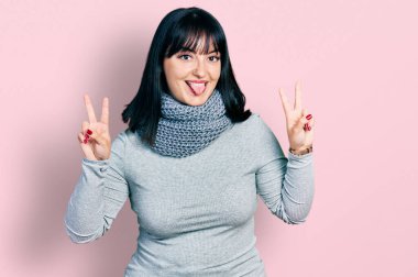 Kış eşarbı takan, ağzı açık gülümseyen, zafer işareti yapan genç İspanyol artı boyunda bir kadın. İki numara.. 