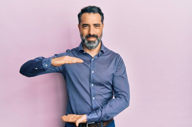 Orta yaşlı, sakallı, gri saçlı, iş kıyafetleri giyen, elleri büyük ve büyük boy işareti gösteren orta yaşlı bir adam. Ölçü sembolü. Kameraya bakıp gülümsüyor. ölçüm kavramı. 