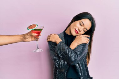 Seksi parti ceketi giyen ve İspanyol kolu olan genç bir kız kokteyl içmeyi teklif ediyor mutlu ve pozitif, kendinden emin gülümseyen. Sevgi ve özgüven. 