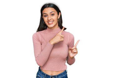 Gündelik kıyafetler giyen, gülümseyen ve kameraya bakan genç İspanyol kız iki eliyle ve parmaklarıyla kenarı işaret ediyor.. 