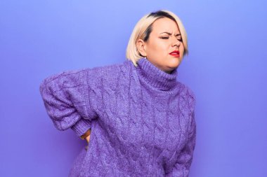 Güzel sarışın ve cüsseli bir kadın. Mor arka planda balıkçı yaka kazak giyiyor. Sırt ağrısı çekiyor.