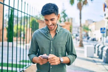 Genç Latin adam mutlu bir şekilde gülümsüyor ve şehirde akıllı telefon kullanıyor..