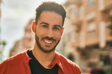 Genç İspanyol adam gülümseyerek şehirde mutlu mesut dikiliyor..