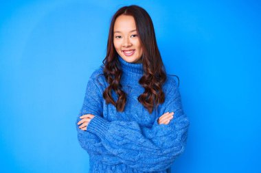 Kış süveteri giyen, kollarını kavuşturup kameraya gülümseyen genç, güzel Çinli bir kız. pozitif kişi. 