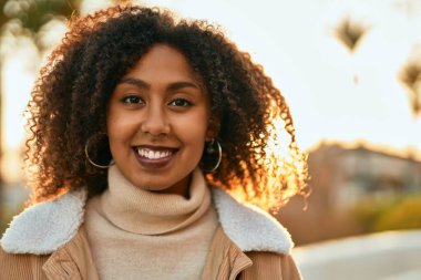 Genç Afrikalı Amerikalı kadın gülümseyerek şehirde mutlu mesut duruyor..