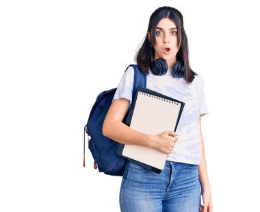 Sırt çantası taşıyan genç ve güzel bir kız. Elinde not defteri var. Korkmuş ve ağzı açık bir şekilde hayrete düşmüş. 