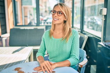 Kahvecinin terasında mutlu mutlu gülümseyen genç sarışın kadın..