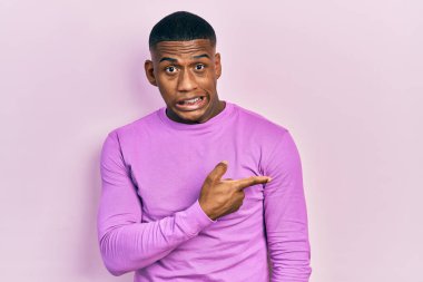 Genç siyah bir adam pembe bir süveter giyiyor endişeli ve gergin bir şekilde işaret ediyor. 