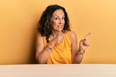 Masada oturan orta yaşlı, güzel bir kadın endişeli ve endişeli bir ifadeye sahip endişeli bir şekilde endişeli bir kenara bakıyor. 