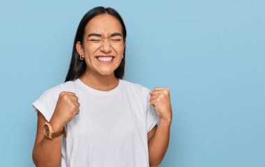 Sıradan beyaz tişörtler giyen Asyalı genç bir kadın başarı için heyecanlı kolları havada ve gözleri kapalı zaferi kutlarken gülümsüyor. Kazanan konsept. 