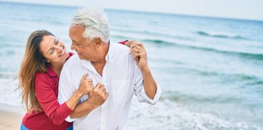 Orta yaşlı İspanyol çift mutlu bir şekilde gülüyor ve kumsalda yürüyorlar.