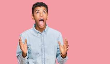 Genç, yakışıklı, Afro-Amerikalı sıradan kıyafetler giyen çılgın ve kızgın bir adam agresif bir ifadeyle bağırıyor ve kollarını kaldırıyor. hüsran kavramı. 