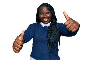 Saçları örgülü, günlük giysiler giyen genç siyahi bir kadın. Elleriyle olumlu bir jest yapıyor. Gülümsüyor ve başarı için seviniyor. kazanan jest. 