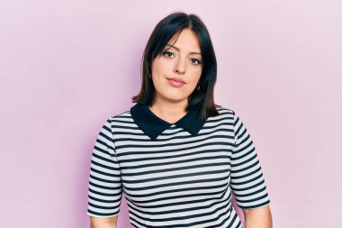 Günlük kıyafetler giyen genç İspanyol kadın yüzünde ciddi bir ifadeyle rahatlamış. Basit ve doğal bir şekilde kameraya bakıyorsun.. 