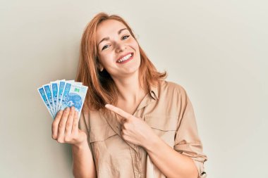 Kafkasyalı genç bir kadın 50 Polonya parası tutuyor. Gülümsüyor, mutlu bir şekilde eli ve parmağı işaret ediyor. 