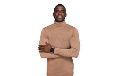 Sıradan bir kazak giyen, kollarını kavuşturup kameraya bakarken gülümseyen genç Afro-Amerikan bir adam. pozitif kişi. 