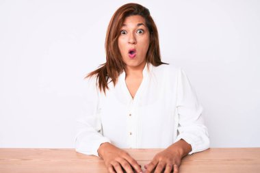 Orta yaşlı esmer, Latin kökenli, beyaz gömlekli bir kadın masada korkmuş ve şok olmuş bir şekilde oturuyor.. 
