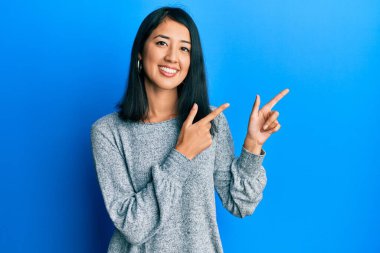 Güzel Asyalı genç kadın, günlük kıyafetler giyip gülümsüyor ve kameraya bakıyor. İki eliyle ve parmaklarıyla kenarı işaret ediyor.. 