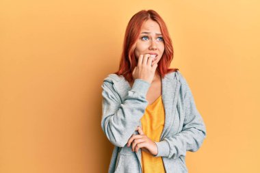 Genç, güzel, kızıl saçlı bir kadın spor bir kazak giyiyor. Stresli ve gergin görünüyor. Elleri ağızdan tırnak yiyor. anksiyete. 