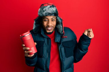 Sakallı, kışlık şapkalı, termosu üstünde kahve tutan, gururla bağıran zafer ve başarıyı kutlayan genç Afrikalı Amerikalı adam. 
