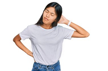 Güzel, beyaz tişört giyen, boynu ağrıyan, eliyle boynuna dokunan, kasları ağrıyan Asyalı bir kadın. 