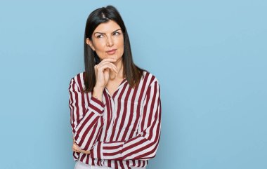 Beautiful brunette woman wearing striped shirt with hand on chin thinking about question, pensive expression. smiling with thoughtful face. doubt concept.  clipart