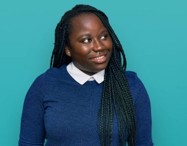 Saçları örgülü genç siyahi bir kadın yüzünde gülümsemeyle yan yana bakıyor, doğal bir ifade. Kendinden emin gülen. 