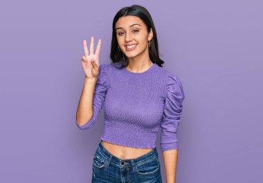 Gündelik kıyafetler giyen genç İspanyol kız üç numarayı gösterip işaret ederken kendinden emin ve mutlu bir şekilde gülümsüyor.. 