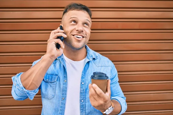 Νεαρός Καυκάσιος Άνδρας Χαμογελά Χαρούμενος Μιλώντας Στο Smartphone Και Πίνοντας — Φωτογραφία Αρχείου