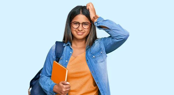 学生のバックパックを着て本を持っている若いラテン語の女の子は混乱し 疑問に思っています 疑いもなく頭に手を置いて考える 包括的な概念は — ストック写真