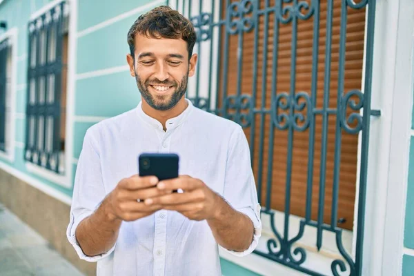 白いシャツを着た髭を生やしたハンサムな男が晴れた日に笑顔で屋外で幸せスマートフォンを使用して — ストック写真