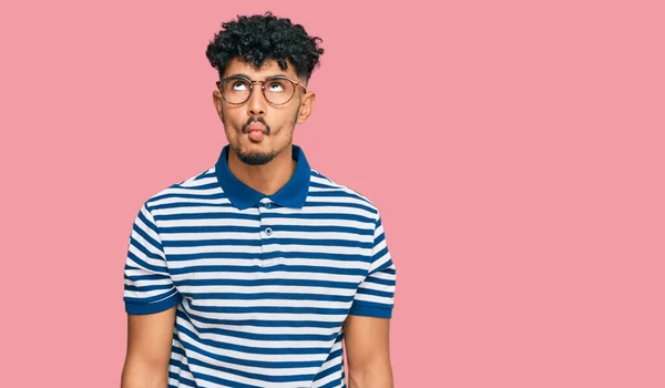 狂気とコミカルなジェスチャーで魚の顔を作るカジュアルな服や眼鏡を身に着けている若いアラブ人の男 面白い表現 — ストック写真