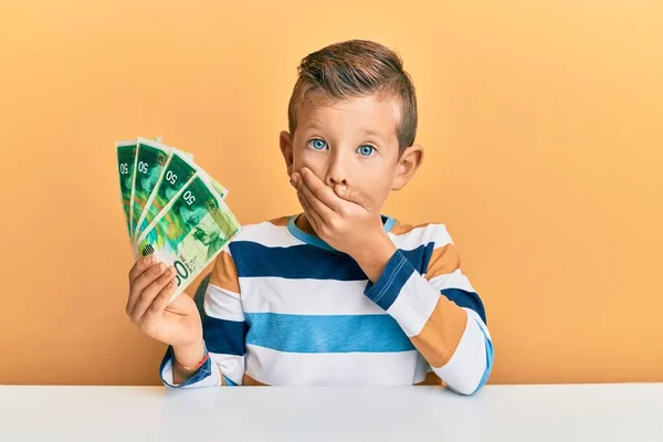 Adorable Caucasian Kid Holding Israel Shekels Sitting Table Covering Mouth — Stock Photo, Image