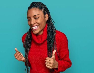 Sıradan bir kazak giyen Afrikalı Amerikalı kadın çok mutlu ve heyecanlı, kolları havada, gülümseyen ve başarı için bağıran kazanan bir jest yapıyor. kutlama konsepti. 